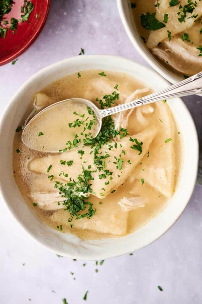 A bowl of Cracker Barrel Chicken and Dumplings soup garnished with chopped parsley.