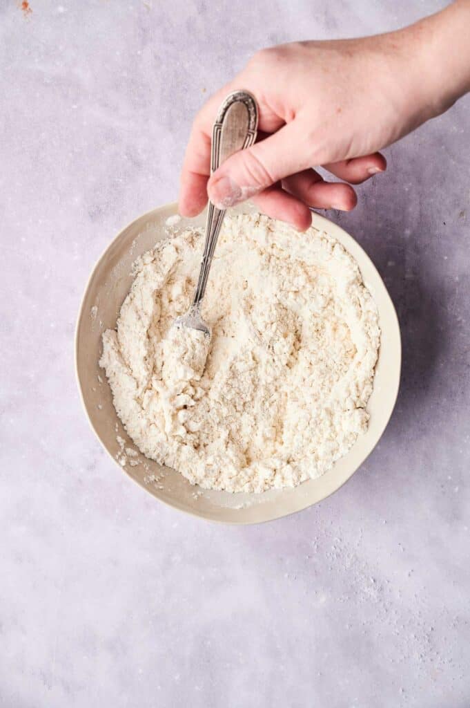 A person mixing ingredients for Cracker Barrel Chicken and Dumplings in a bowl with a spoon.