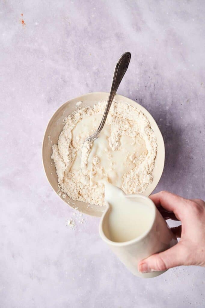 Pouring milk into a bowl of flour mixture for Cracker Barrel Chicken and Dumplings.