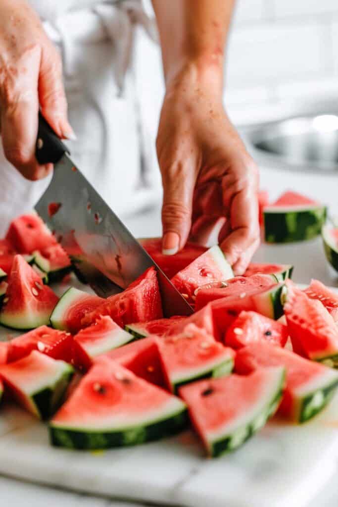 A person cutting watermelon on a cutting board.