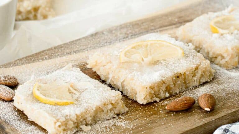 Slices of lemon bars with almond garnish on a wooden surface, dusted with powdered sugar.