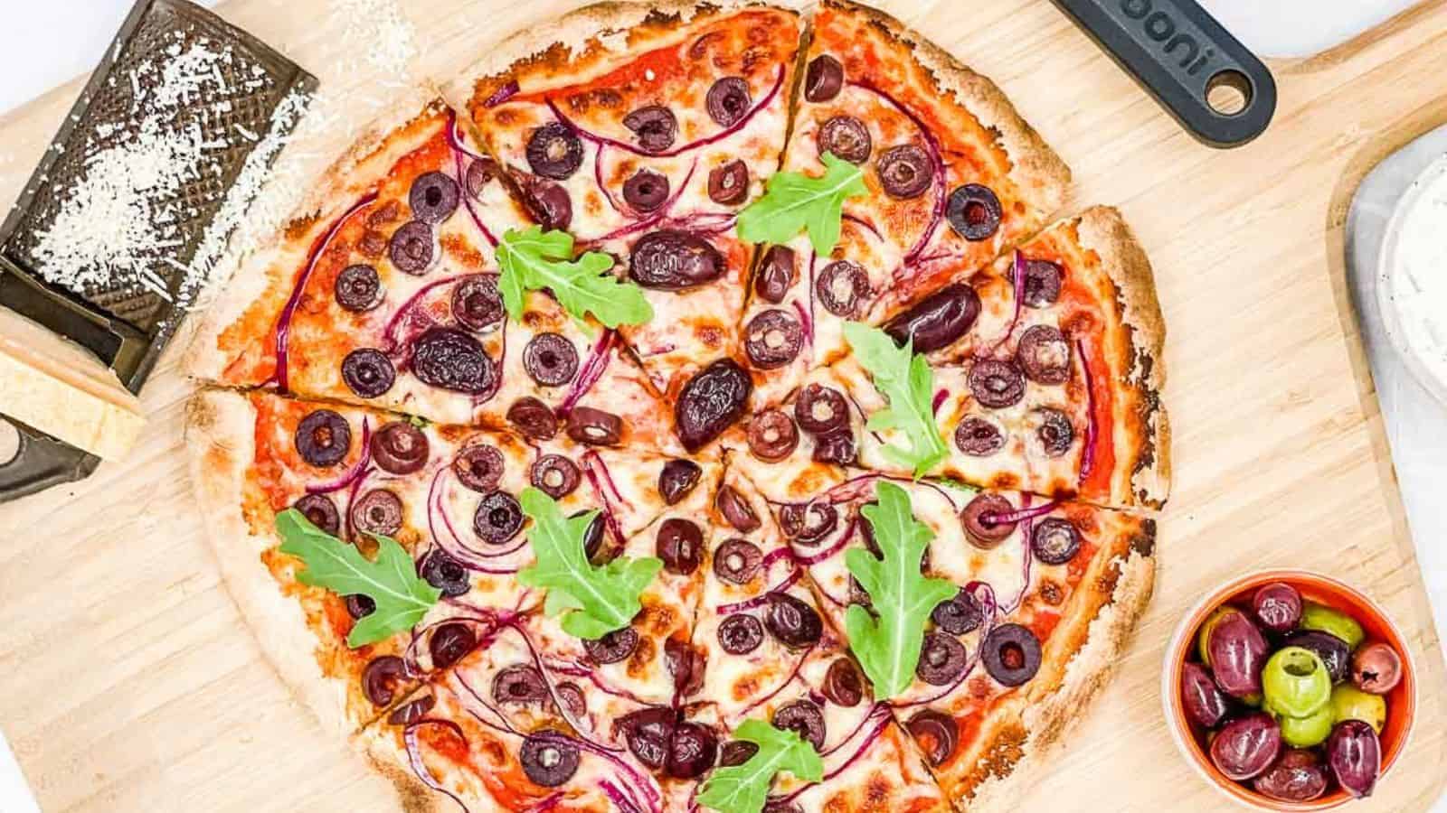 Cooked olive pizza on a pizza paddle.