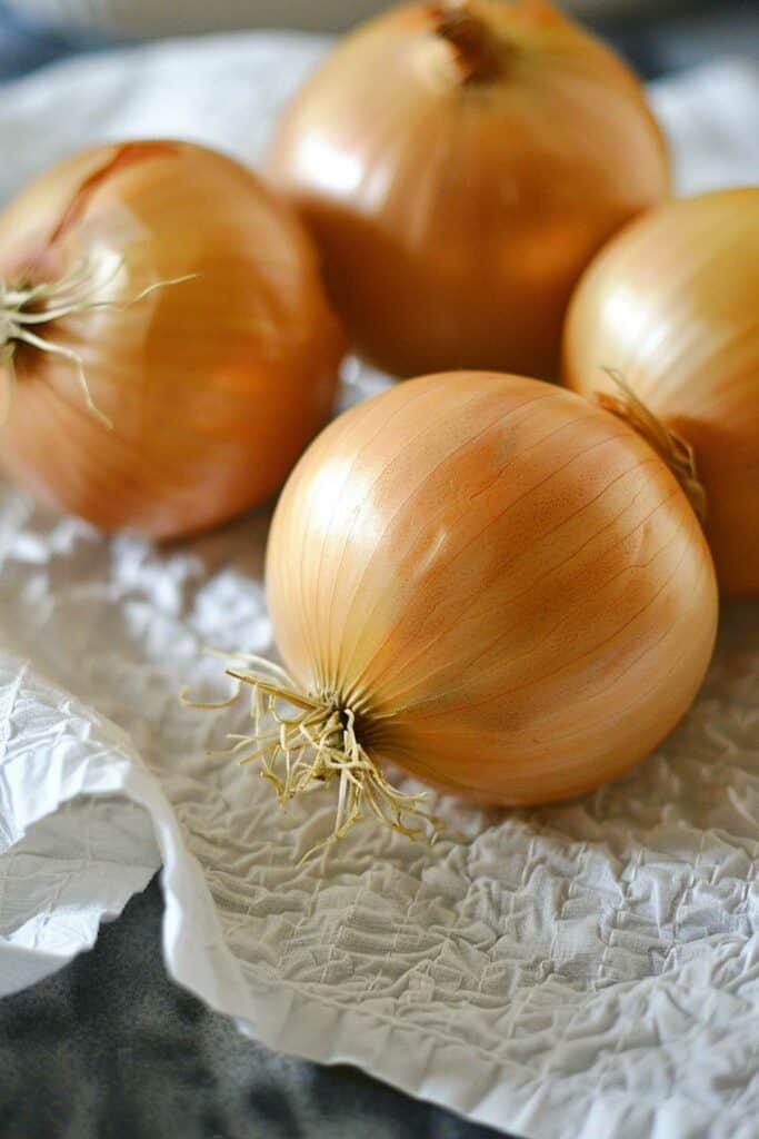Three whole onions on a crinkled white paper surface.