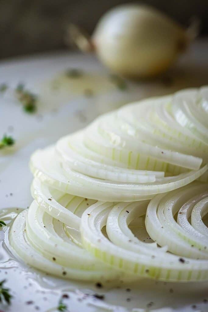Sliced white onion arranged on a plate with herbs and a whole onion in the background.