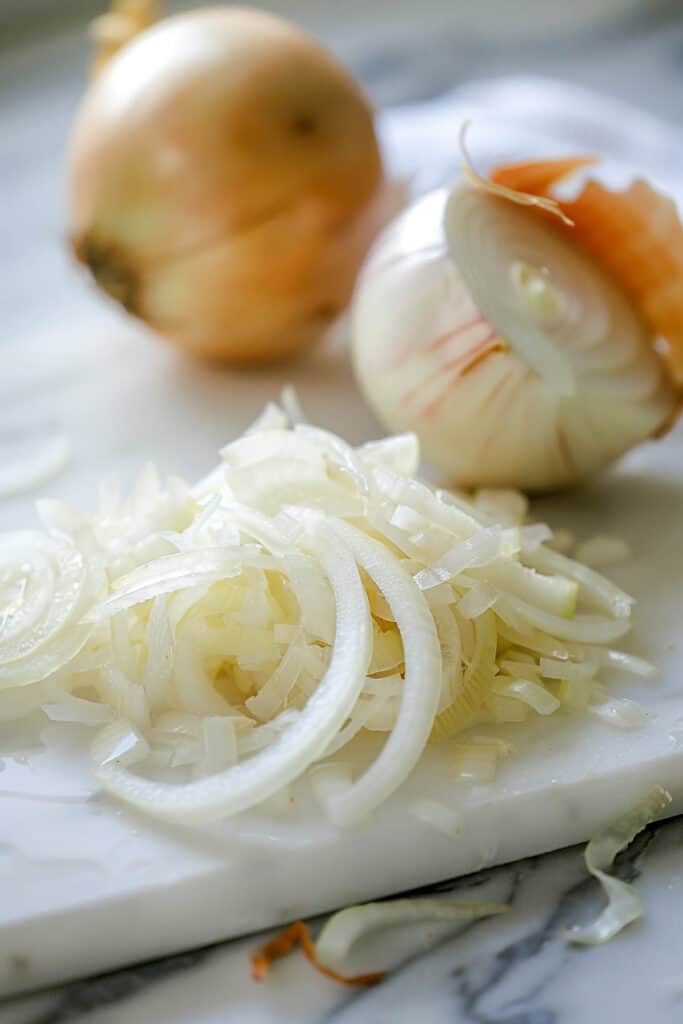 Sliced and whole onions on a kitchen cutting board.