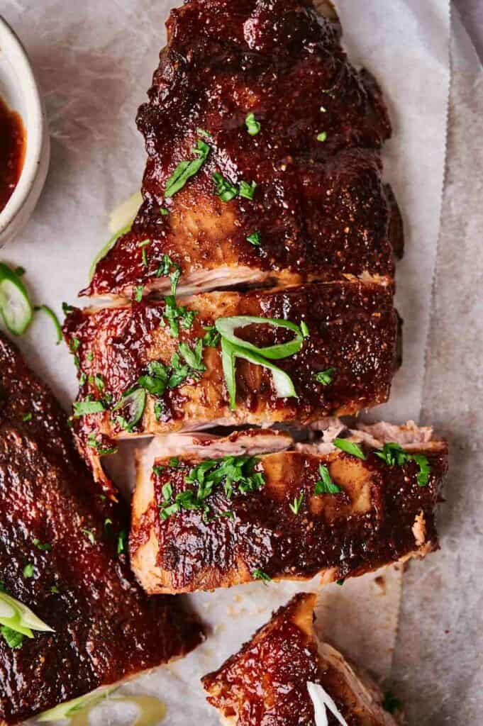 Oven-baked glazed barbecue ribs garnished with chopped herbs on parchment paper.