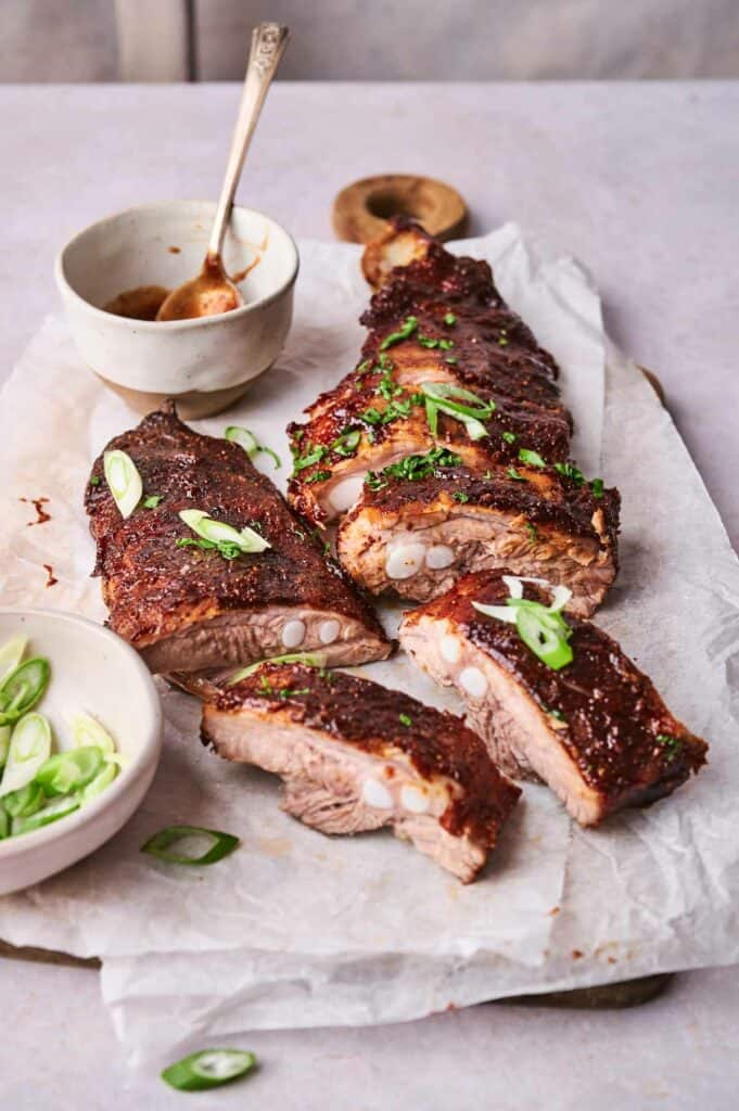 Sliced oven-baked barbecue pork ribs garnished with green onions on parchment paper.