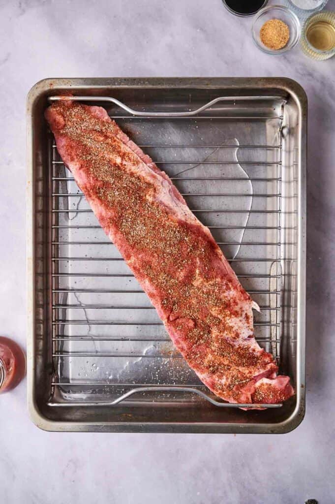 A seasoned oven-baked ribs on a baking sheet with a rack, ready for cooking.