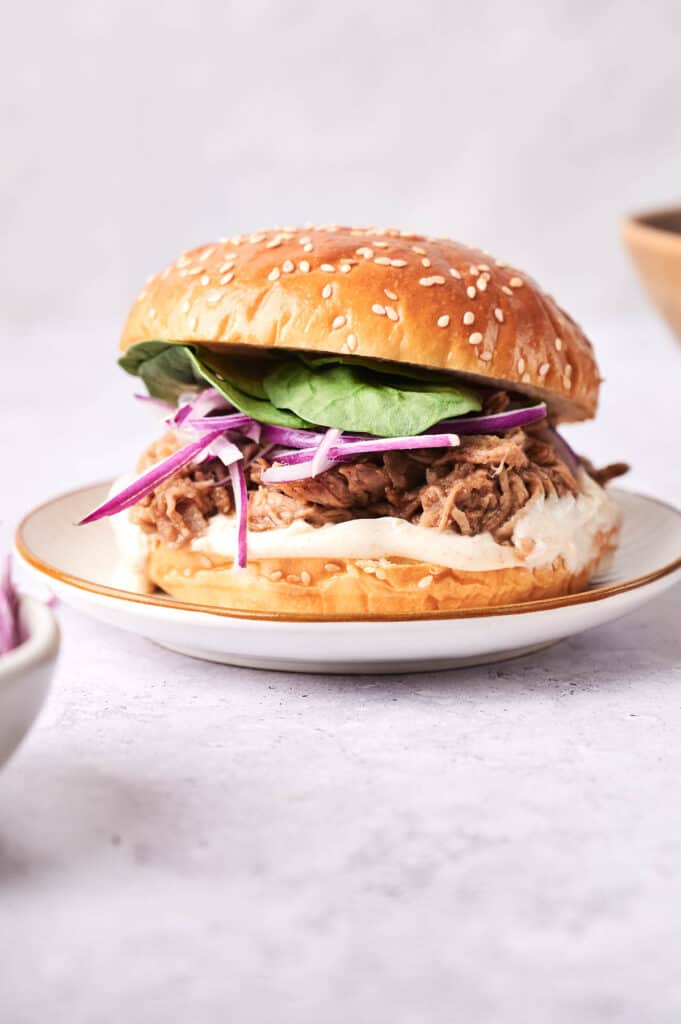 A slow cooker pulled pork sandwich with coleslaw and spinach on a sesame seed bun, served on a plate.