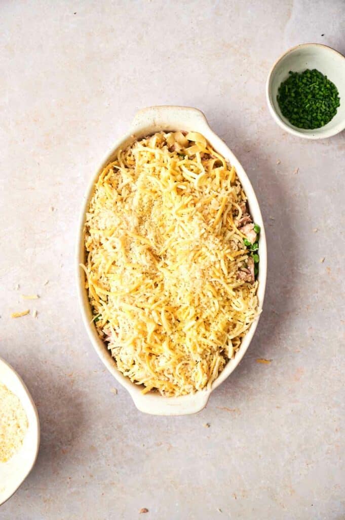 tuna casserole ingredients mixed in a baking dish with cheese on top.