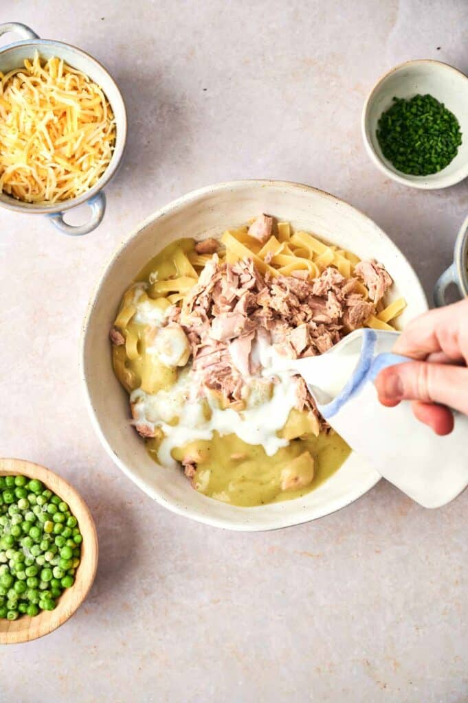 Someone pouring milk into the bowl with pasta.