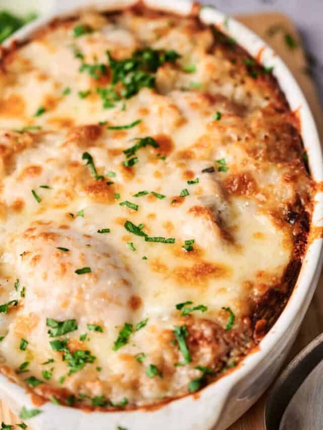 A close-up of a baked dish with melted cheese and garnished with chopped green herbs, served in a white round dish.