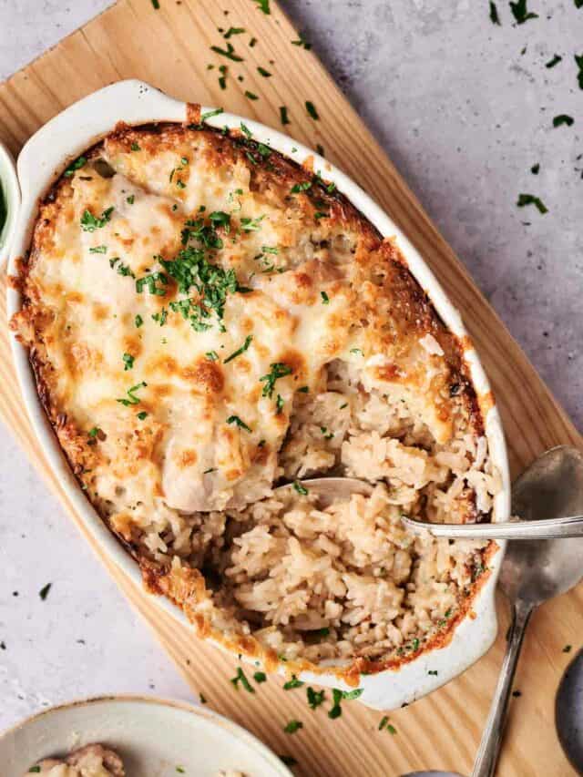 A ceramic dish containing baked rice casserole topped with melted cheese and garnished with chopped parsley, with a spoon on the side.