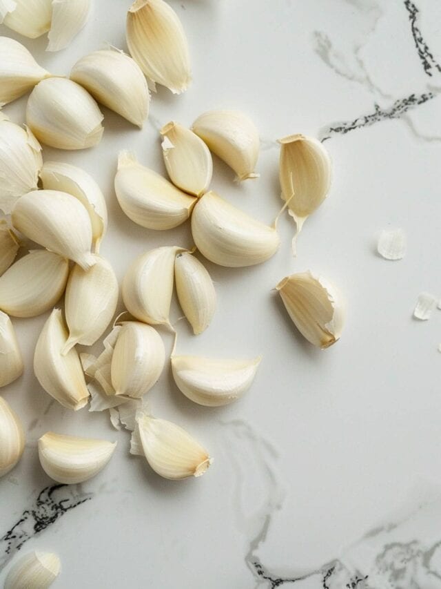 A cluster of garlic cloves scattered on a marble surface.
