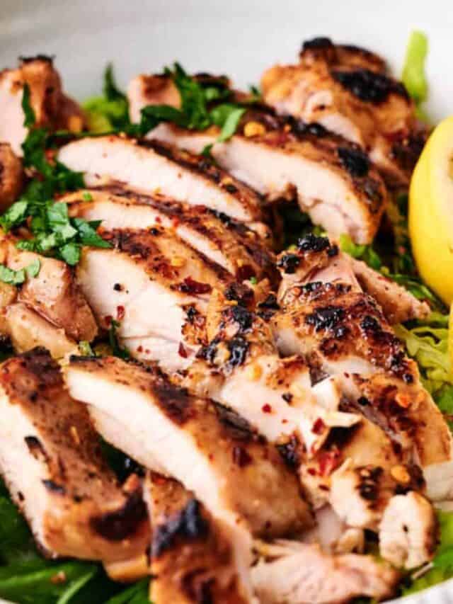 Sliced grilled chicken breast garnished with herbs and accompanied by a lemon wedge.