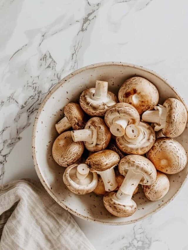 A bowl of fresh mushrooms on a marbled surface.