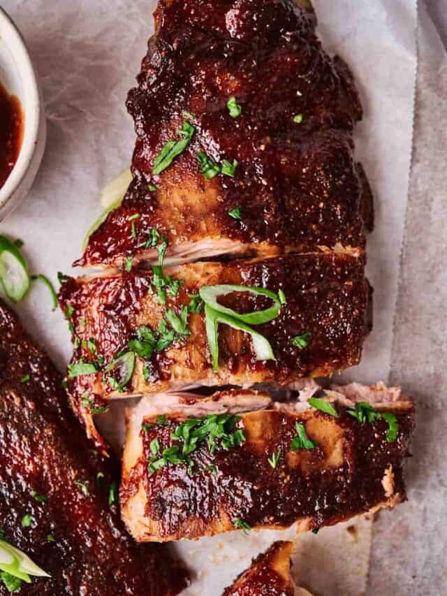 Oven-baked glazed barbecue ribs garnished with chopped herbs on parchment paper.
