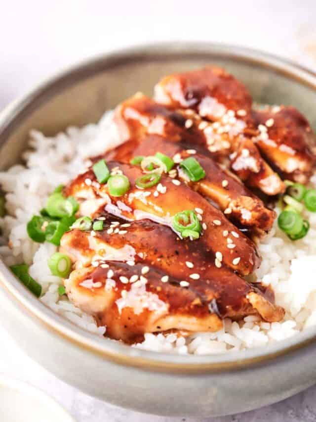 A bowl of white rice topped with slices of glazed meat, garnished with green onion and sesame seeds.