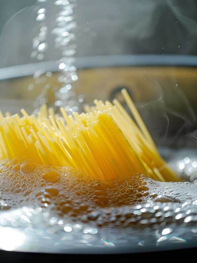 Uncooked spaghetti boiling in a pot with rising steam and water bubbles.