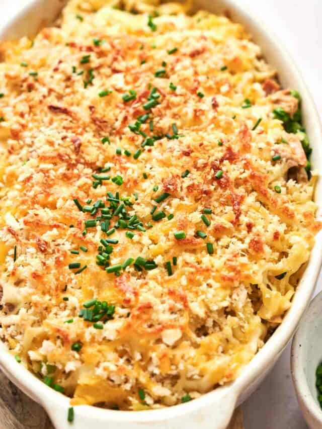 A baked casserole with creamy, cheesy pasta topped with golden breadcrumbs and garnished with chopped chives in a white dish.