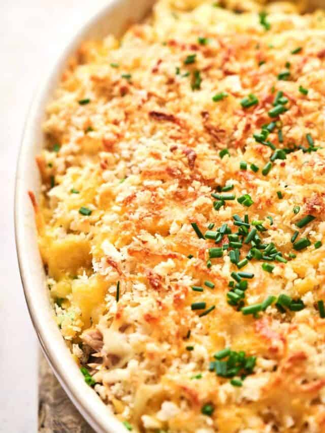 Baked macaroni and cheese in a white oval dish, topped with golden breadcrumbs and garnished with chopped chives.