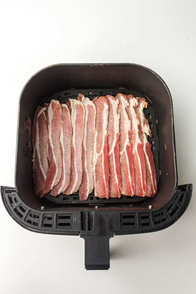 Bacon strips layered in the air fryer basket.
