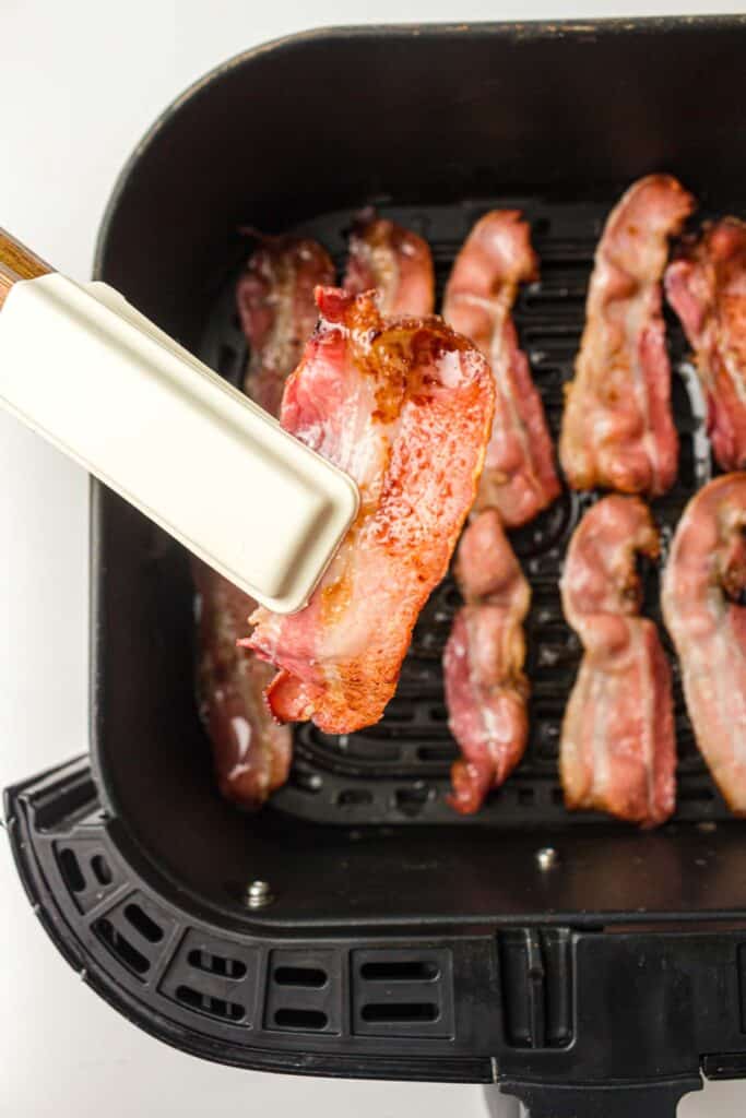 Bacon strip being lifted with a tong.