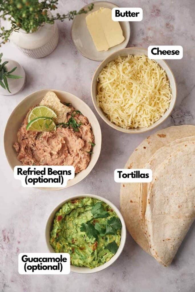 Ingredients for making tacos displayed on a countertop, including tortillas, cheese, butter, refried beans, and guacamole, each labeled accordingly.