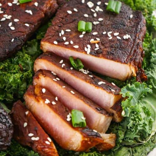 Asian style pork chops garnished with sesame seeds and green onions, served on a bed of kale.
