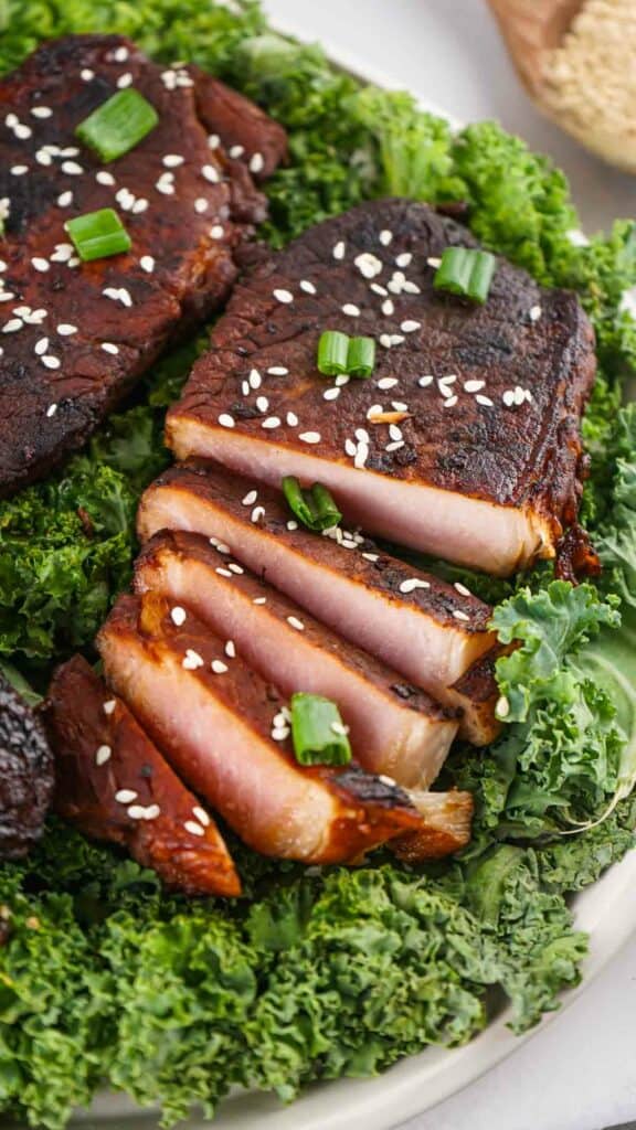 Asian style pork chops garnished with sesame seeds and green onions, served on a bed of kale.