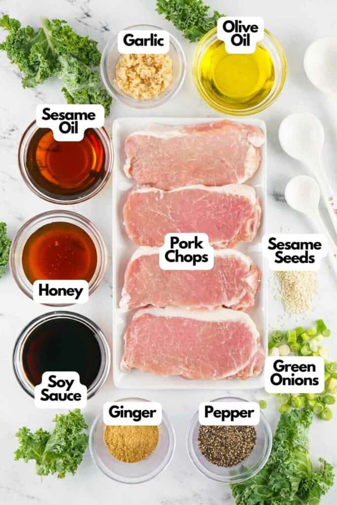 Ingredients for an Asian-style pork chop recipe including pork chops, sesame oil, honey, soy sauce, olive oil, garlic, ginger, sesame seeds, green onions, and pepper on a kitchen countertop
