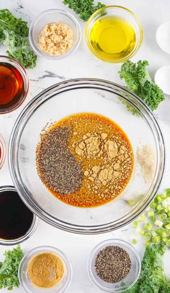 Ingredients for an Asian-style dressing in small bowls and a glass bowl with mixed liquids and spices, arranged on a marble surface.