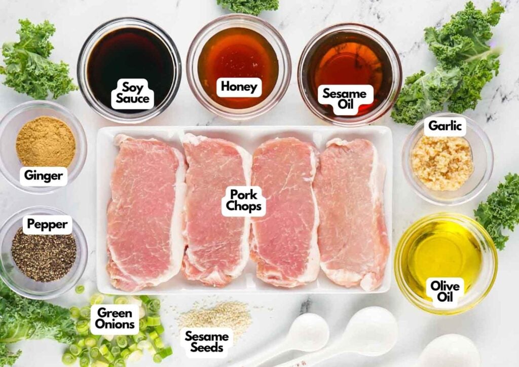 Top-down view of raw asian style pork chops surrounded by labeled bowls of soy sauce, honey, sesame oil, garlic, olive oil, ginger, pepper, green onions, and sesame seeds on a white surface.
