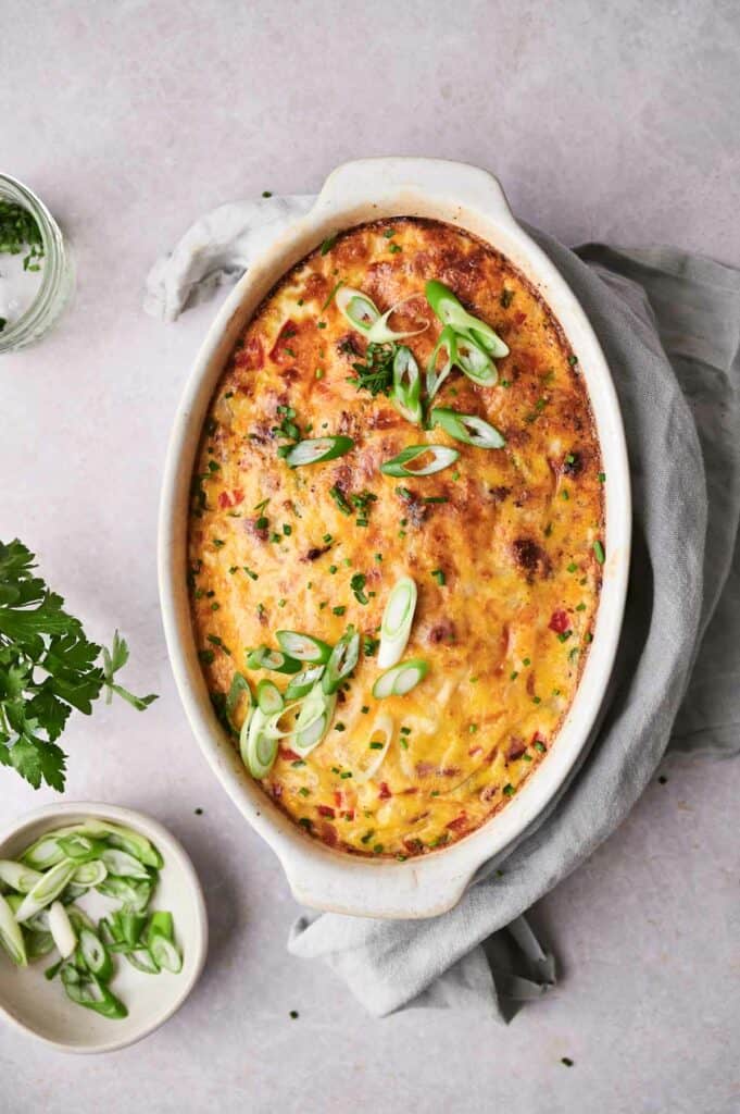 Oval breakfast casserole dish with baked gratin topped with green onions on a light background.