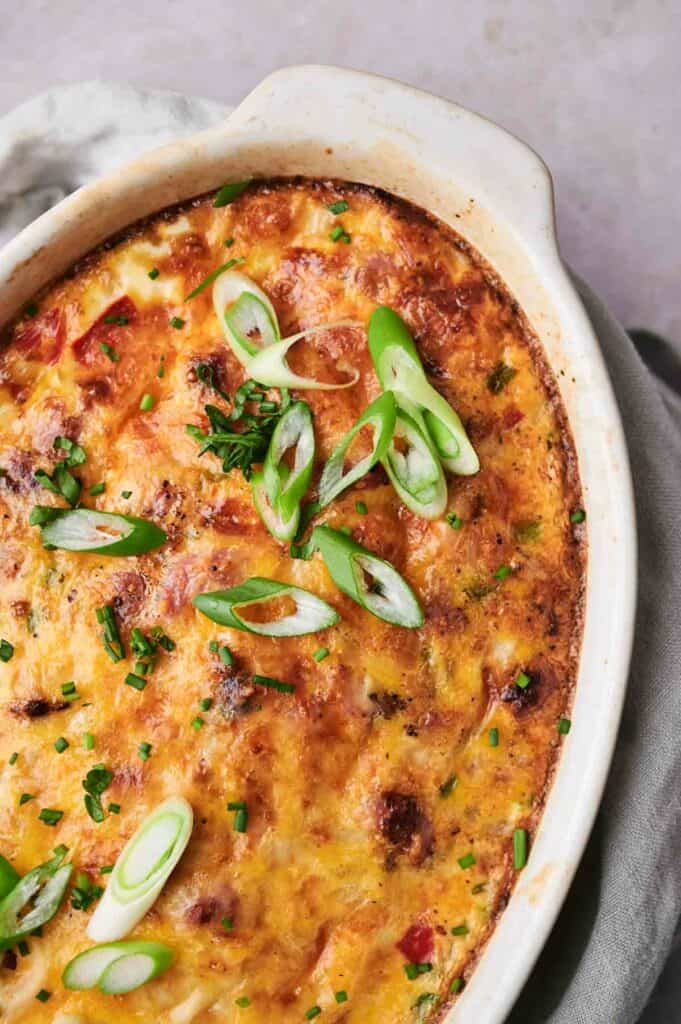 A freshly baked breakfast casserole with melted cheese and garnished with green onions and herbs.