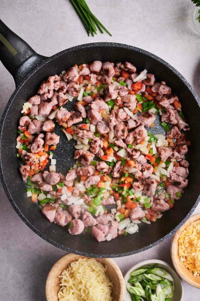 Sautéed diced vegetables and sausage cooking in a skillet for a breakfast casserole.