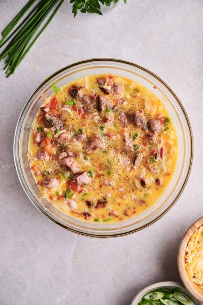 A bowl of creamy breakfast casserole garnished with herbs and spices, accompanied by shredded cheese and fresh greens on the side.