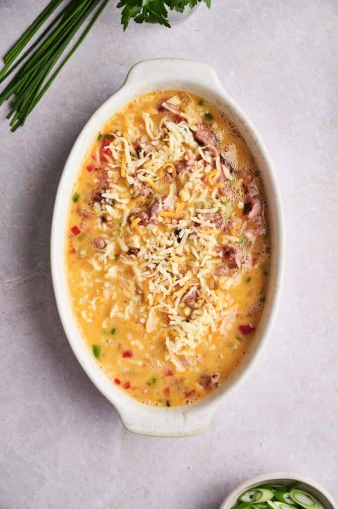 A bowl of creamy breakfast casserole garnished with shredded cheese on a light surface.