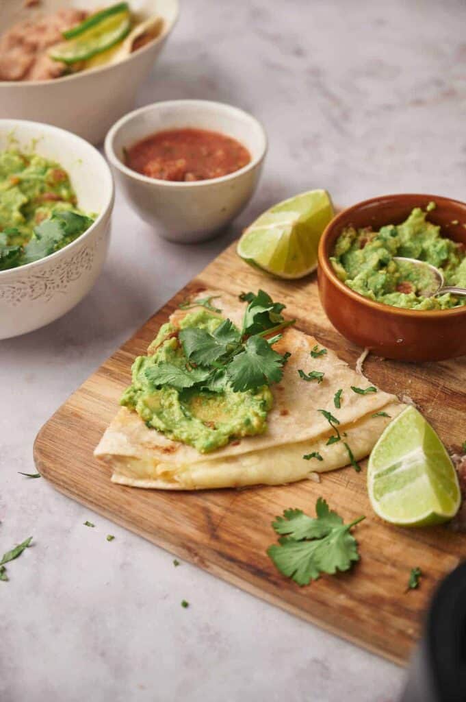 Guacamole served on flatbread, garnished with cilantro, accompanied by lime wedges and bowls of salsa.