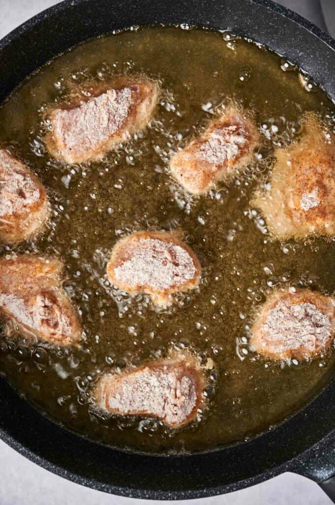 Breaded Chick-fil-A chicken nuggets frying in oil in a black skillet.