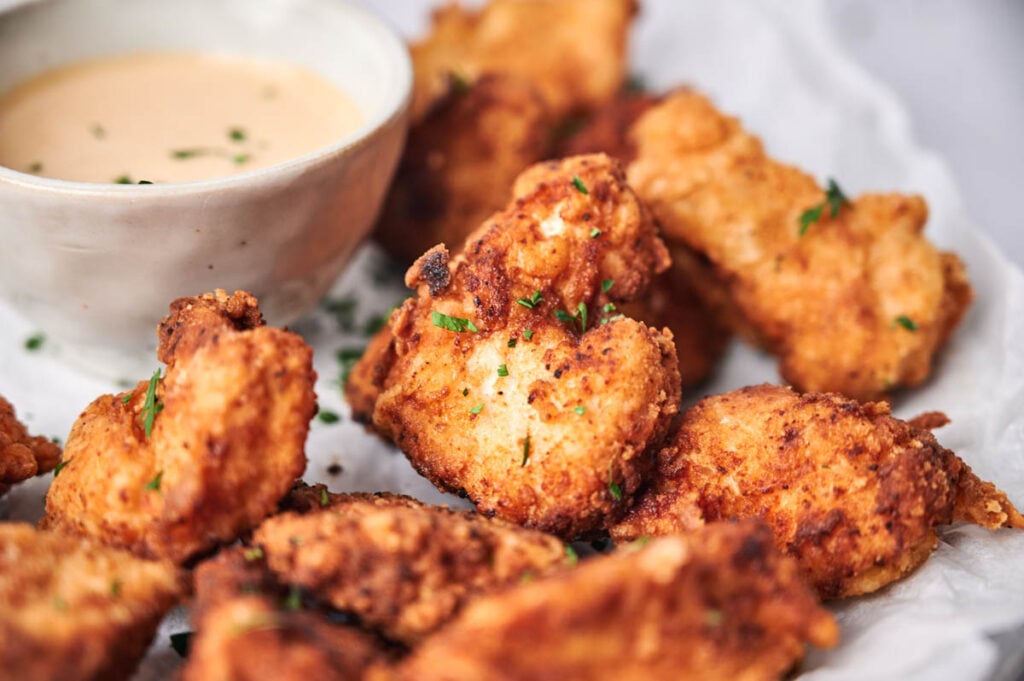 Close-up of crispy Chick-fil-A chicken nuggets, garnished with herbs and served on parchment paper with a bowl of dipping sauce in the background.