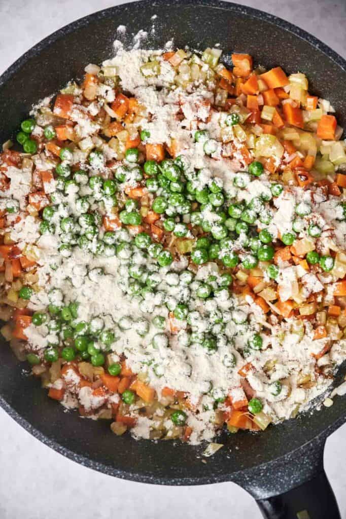 Vegetables and flour in a frying pan, likely being prepared for a chicken pot pie.