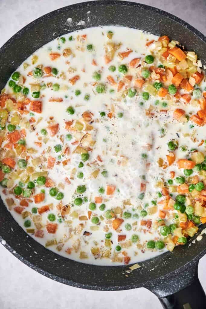 Diced vegetables simmering in a creamy, milk-based sauce alongside chunks of chicken in a skillet for Chicken Pot Pie.