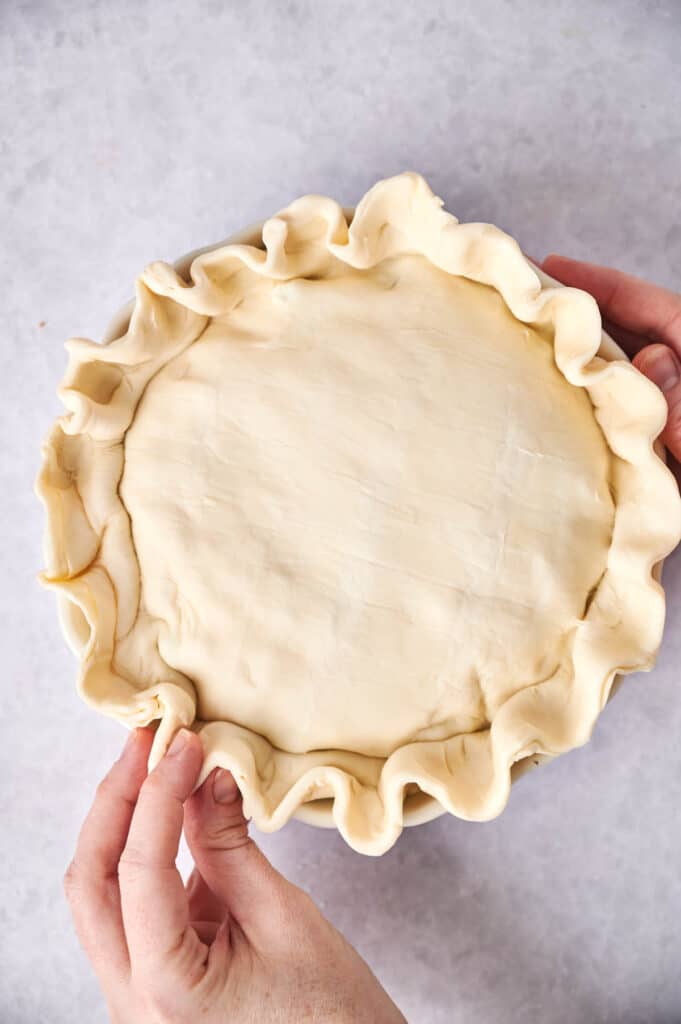 Unbaked chicken pot pie crust in a dish held by two hands.