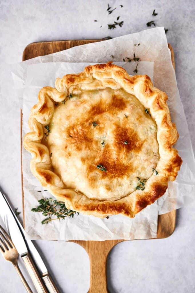 A freshly baked chicken pot pie on a cutting board, garnished with herbs.