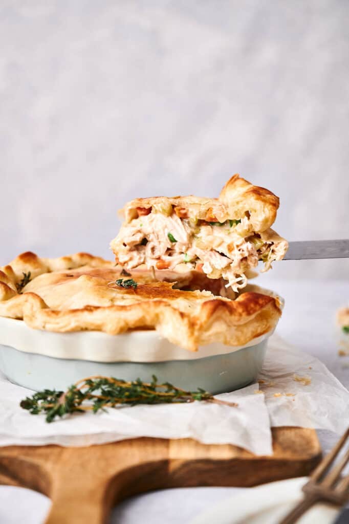 A slice of Chicken Pot Pie being lifted from the dish reveals the creamy filling speckled with herbs.