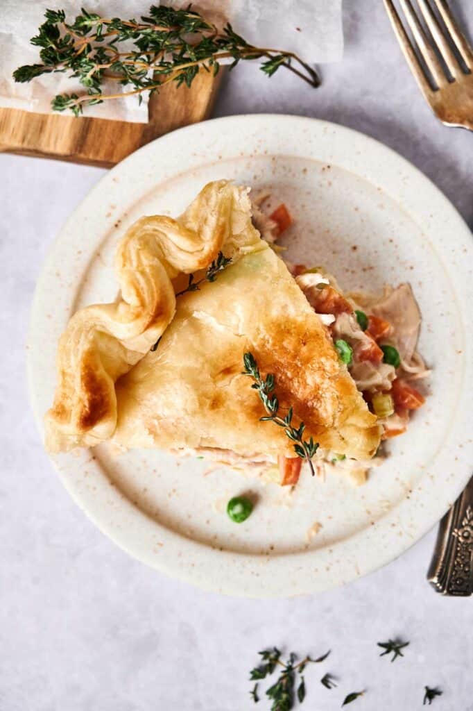 Chicken Pot Pie on a plate, garnished with thyme, with cutlery and herbs on the side.