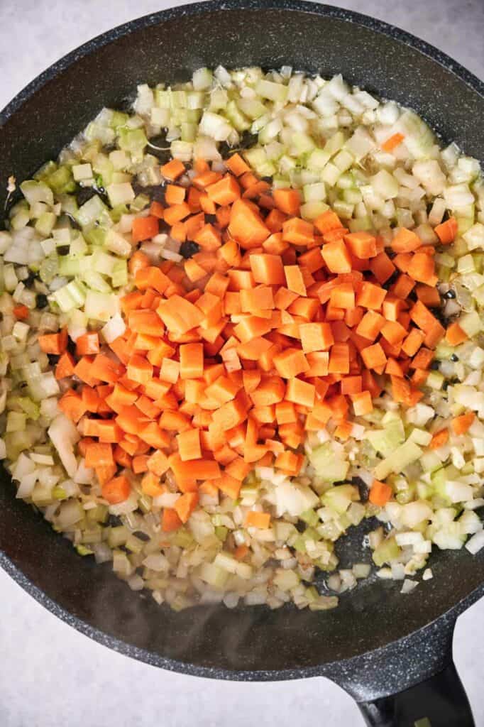 Diced onions, carrots, and celery sautéing in a pan for Chicken Pot Pie.