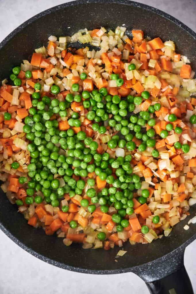 Diced onions, carrots, and peas sautéing in a frying pan for Chicken Pot Pie.