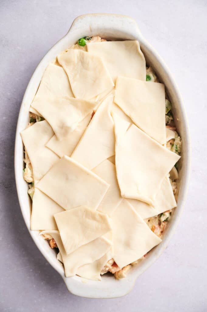 An oven dish filled with a creamy chicken pot pie casserole topped with uncooked lasagna sheets arranged in a patchwork pattern.